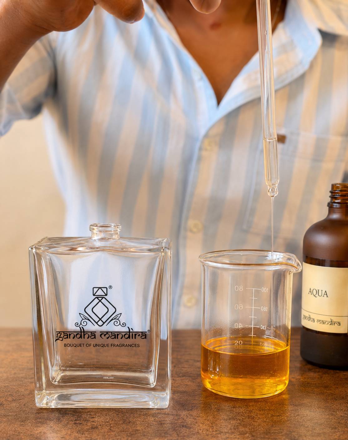 Pipette dispensing aqua essence into a beaker beside a Gandha Mandira bottle