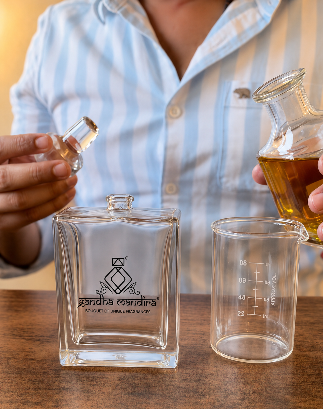 Perfumer holding a glass stopper beside a Gandha Mandira bottle and amber oil decanter